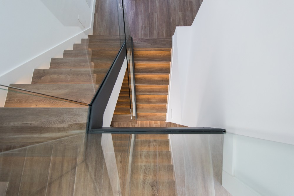 Escalera moderna de madera con barandilla de cristal y diseño minimalista en vivienda en Madrid