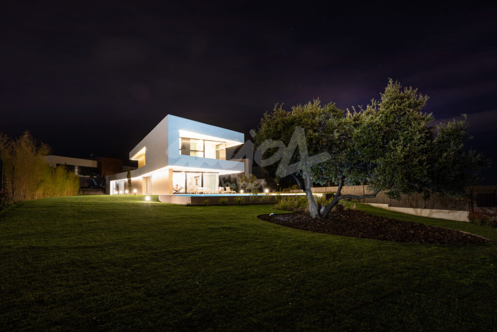 Vista nocturna de vivienda de lujo con iluminación arquitectónica y amplio jardín en urbanización exclusiva de Madrid