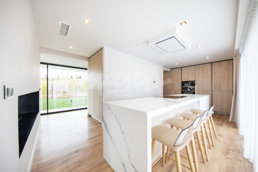 Cocina moderna de diseño con isla central, acabados en madera y encimera blanca en vivienda de lujo en Madrid