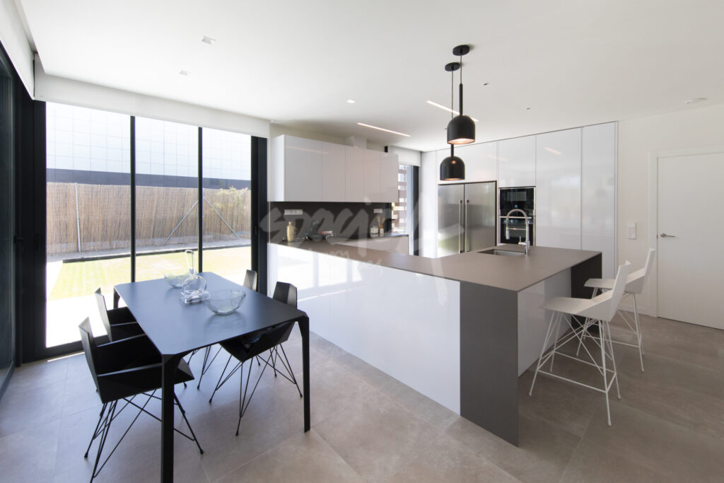 Cocina moderna con isla en tonos neutros, muebles blancos y encimera oscura