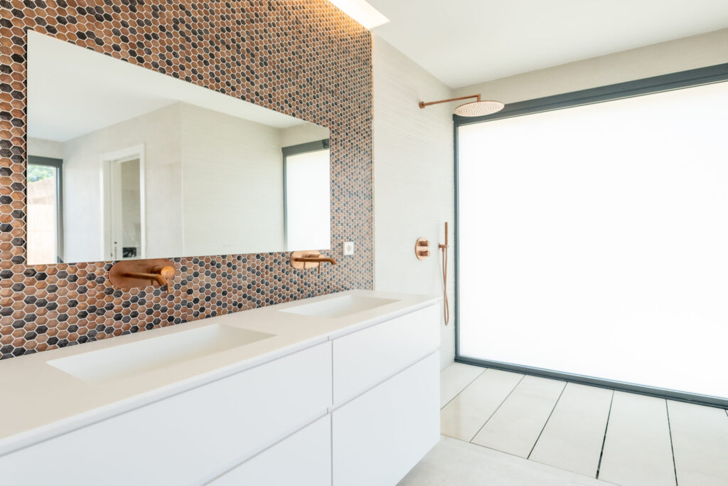 Baño con ducha revestida en mosaico cerámico hexagonal y grifería empotrada en vivienda ZOE44
