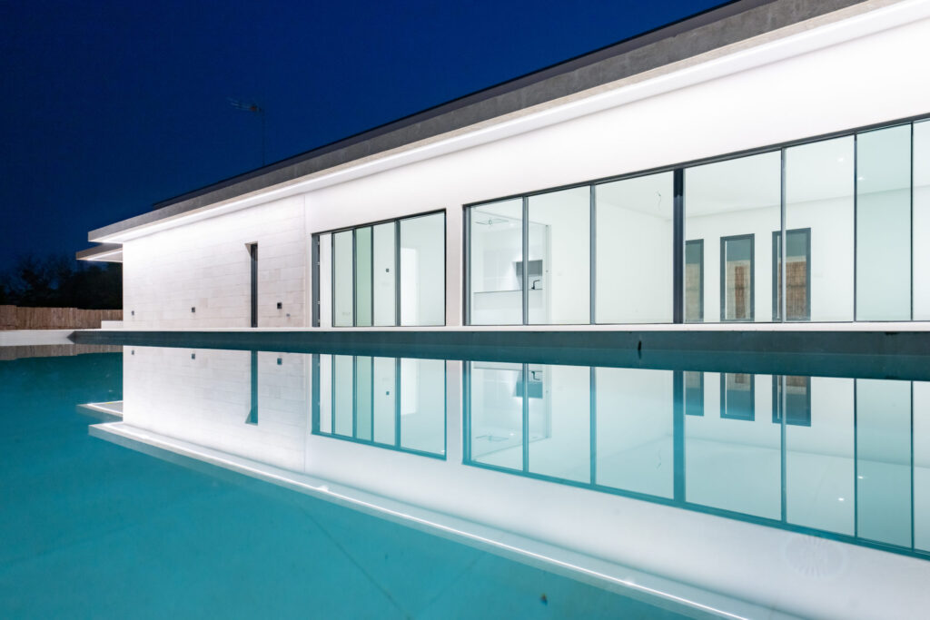 Vivienda contemporánea ZOE44 con piscina y grandes ventanales iluminados durante la noche
