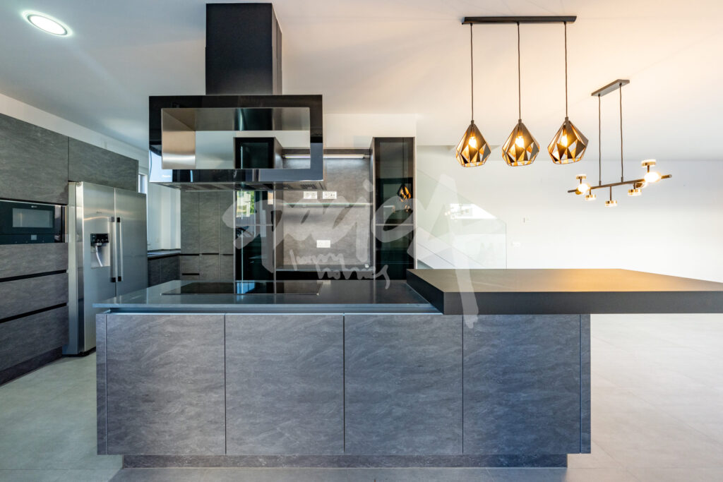 Cocina contemporánea con isla central, electrodomésticos integrados, campana de diseño y sistemas tecnológicos avanzados