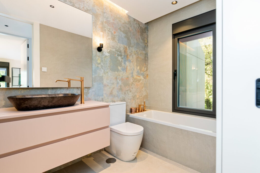 Baño pequeño de diseño moderno con lavabo suspendido, bañera compacta, luz natural y acabados en tonos neutros