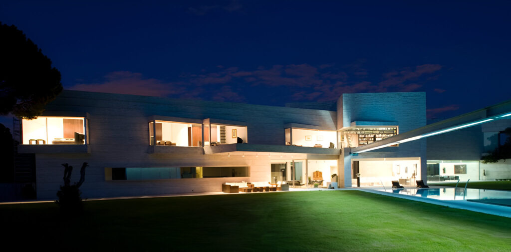 Vivienda unifamiliar de lujo iluminada de noche con jardín, piscina y amplios espacios exteriores