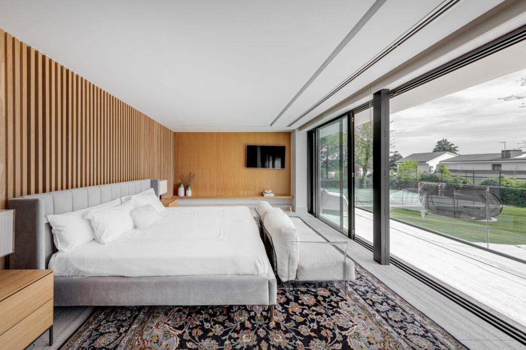 Dormitorio principal moderno con panelado de madera, cama tapizada y salida al jardín