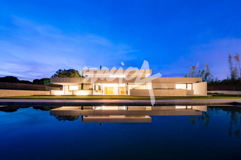 Casa moderna de diseño horizontal iluminada de noche con reflejo en piscina o lámina de agua