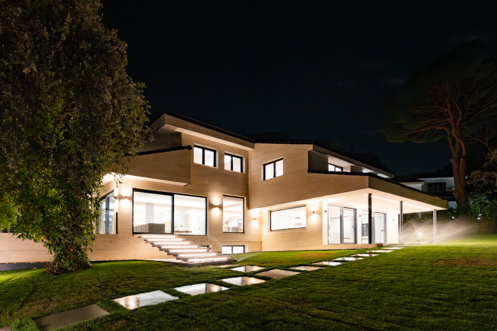 Vivienda contemporánea de noche con jardín iluminado, grandes ventanales y arquitectura moderna en calle Poniente