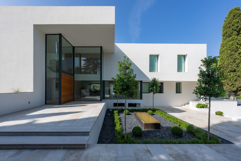 Vivienda unifamiliar moderna de líneas rectas, fachada blanca y grandes ventanales con jardín minimalista